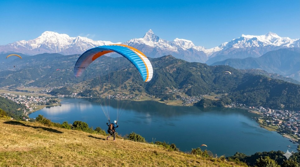Paraglider launching from Sarangkot Hill with Phewa Lake and the Annapurna range visible in the background.